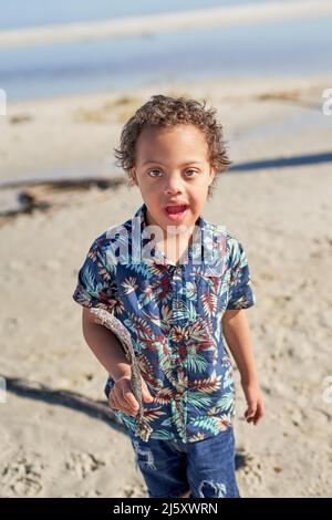 Retrato lindo niño con síndrome de Down sujetando palo en la playa
