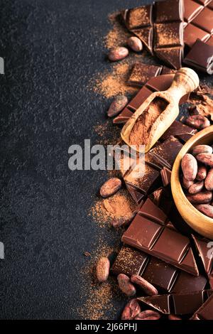 Chocolate . Composición del cacao en polvo, barras de cacao rallado y de frijol y trozos de leche y chocolate negro sobre fondo negro. Cocción de col Foto de stock