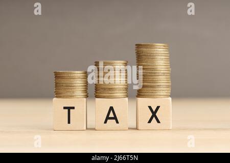 Palabra de impuesto en bloques de madera con monedas apiladas en pilas crecientes. Concepto de aumento de impuestos. Espacio de copia Foto de stock