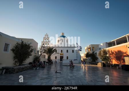 Oia, Grecia - 11 de mayo de 2021 : Vista de los locales, turistas y niños jugando frente a una pintoresca iglesia en el centro de Oia Santorini Foto de stock