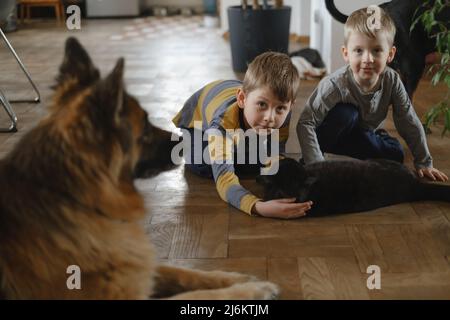 Los niños jugando, acariciando el gato negro mientras el perro pastor alemán está sentado cerca de casa. Los niños tienen mascotas y se ocupan de ellas