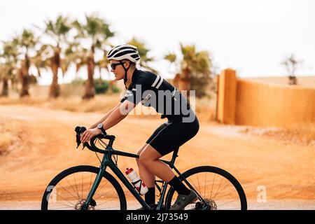 Vista lateral de jovencita ciclista haciendo ejercicio en el campo. Mujer montando su bicicleta profesional. Foto de stock