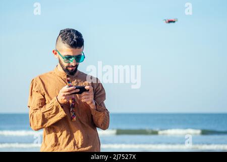 Hombre árabe probando una foto de drone y el vídeo que se dispara en el cuadrocopter sobre el mar en la playa de Goa