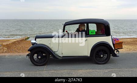 Vintage Cream y Black Austin Seven Motor Car con cesta aparcada en la playa Promenade frente al mar y en el fondo. Foto de stock