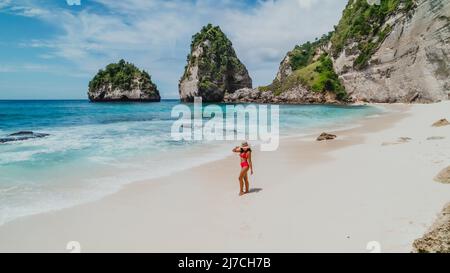 Joven mujer asiática en un bikini rojo en una playa de arena blanca tropical con agua turquesa en Diamond Beach en Nusa Penida Bali Indonesia