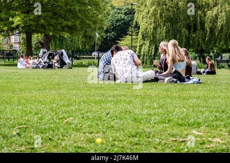 Epsom Surrey, Londres, mayo de 09 2022, Grupos de jóvenes sentados en la hierba en un parque relajante y hablando Foto de stock