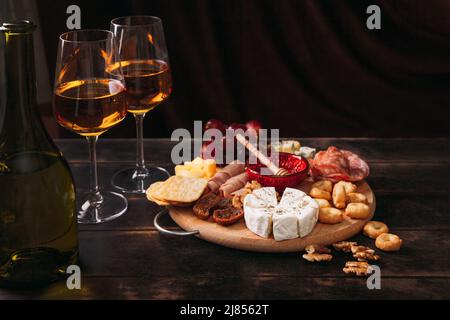 Salchicha y queso cortado con fruta, galletas y salsa con dos vasos de babero blanco y una botella. Charcutería y plato de queso