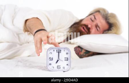 Despertar por la mañana. Hombre dormido barbudo apagando el despertador. Hombre en la cama. Despertar temprano, insomnio. Foto de stock