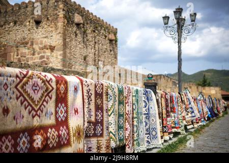 Alfombras hechas a mano colgadas en una pared de piedra - recuerdos turísticos de Georgia y países con cultura oriental