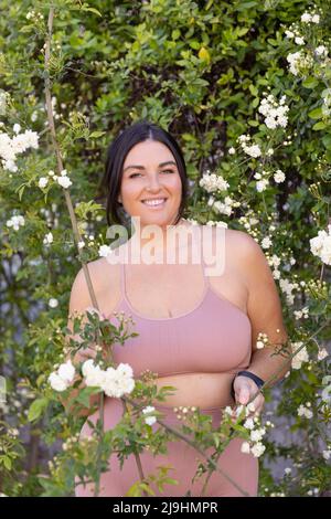 Mujer sonriente más grande de pie en medio de las flores Foto de stock