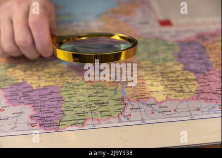 Un hombre sostiene una lupa en su mano sobre un mapa. Un hombre de mediana edad con una lupa en un marco dorado. Los nombres están escritos en ucraniano. Foto de stock