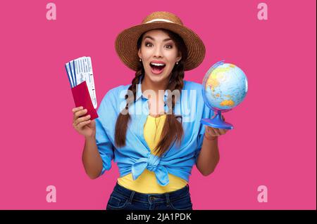 Mujer feliz conmocionada con pasaporte y billete que sostiene el globo en un fondo aislado. Concepto de turismo Foto de stock