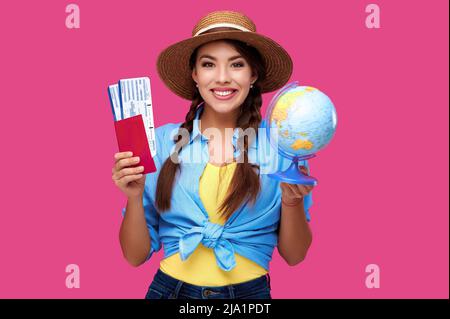 Mujer feliz conmocionada con pasaporte y billete que sostiene el globo en un fondo aislado. Concepto de turismo Foto de stock