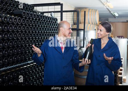 Trabajadores adultos de la bodega que tienen una botella de vino
