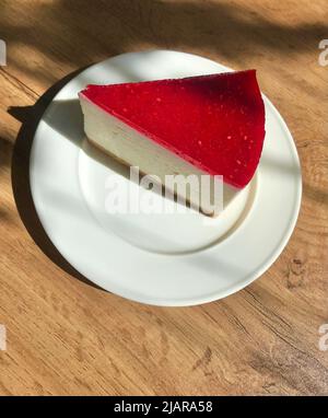 Tarta de queso de frambuesa en un plato blanco. Mesa de madera con sombras. Desayuno en una cafetería. Foto de stock