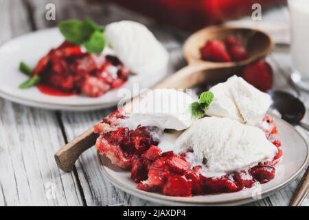 Dulce zapatero casero de fresa o Sonker con helado de vainilla francés sobre una mesa rústica de madera blanca. Enfoque selectivo extremo con backgro borroso Foto de stock