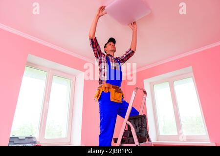 Un electricista instala una lámpara de araña en el techo. Las manos de un electricista están instalando y conectando una lámpara a un techo. Reparación de la luz de techo Foto de stock