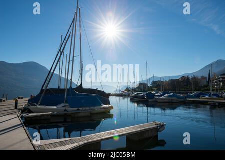 Puerto con buque Náutico en el lago alpino Maggiore con Montaña y Sunbeam en Brissago, Suiza. Foto de stock