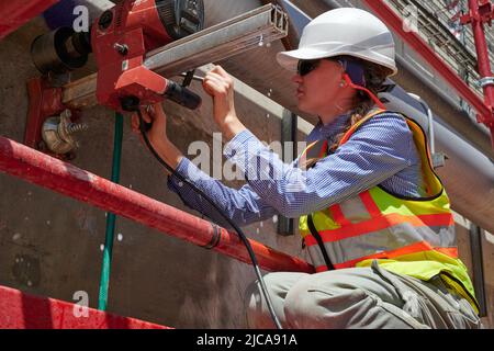 Un Trabajador de la Construcción Femenino Taladrinas de núcleo en una pared de retención de hormigón Foto de stock