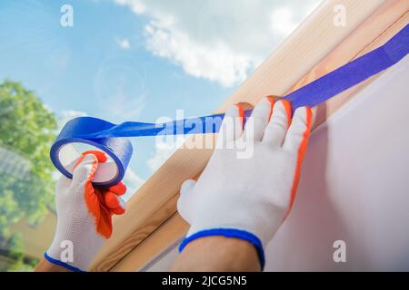 Preparación de las paredes de una sala para trabajos de renovación. El Trabajador de Construcción que usa Guantes de Construcción aplica una Cinta de Pintor Azul a una Pared Antes de Sta. Foto de stock