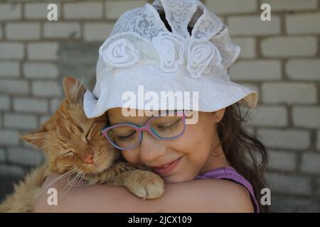 niña pequeña jugar en el jardín de verano con su gato rojo esponjoso Foto de stock