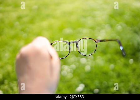 Mala visión, con la mano sujetando las elegantes gafas con montura sobre un fondo verde borroso Foto de stock