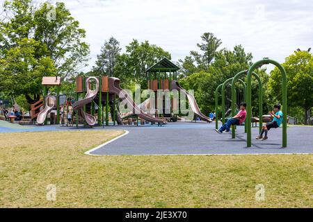 BLOWING ROCK, NC, EE.UU.-20 JUNIO 2022: Patio de recreo en City Park, dos niños juegan en columpios, equipo de patio de recreo y niños en el fondo. Foto de stock