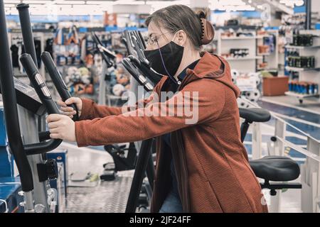 Mujer en una tienda de deportes elige un gran simulador deportivo - cinta de correr para comprar Foto de stock