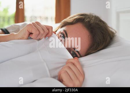 Retrato de una joven mujer mirando desde las colchas de su cama Foto de stock