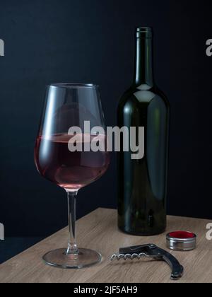 Helsinki / Finlandia - 26 DE JUNIO de 2022: Una botella de vino tinto y una copa y un sacacorchos sobre un fondo oscuro Foto de stock