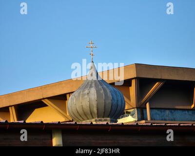 Símbolo de la iglesia ortodoxa en una pequeña cúpula con cielo azul claro y edificios urbanos en el fondo Foto de stock