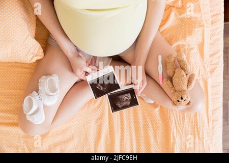 Mujer embarazada sentada en la cama y mirando la foto de su bebé por Ultrasound Scan. Una mujer embarazada muestra su informe de ultrasonido y su bebé por nacer. Foto de stock