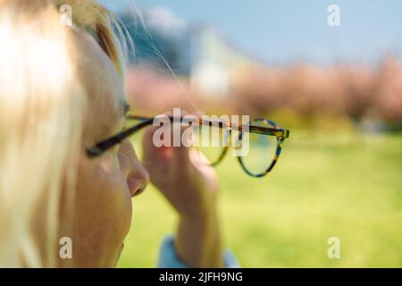 Mala visión, con la mano sujetando las elegantes gafas con montura sobre un fondo verde borroso Foto de stock