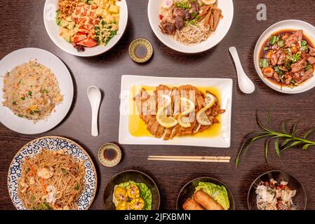 Conjunto de platos asiáticos vistos desde arriba, filetes de pollo empanados con limón, tres delicias de arroz, fideos fritos, rollitos de primavera, takoyaki, ramen de cerdo y po Foto de stock