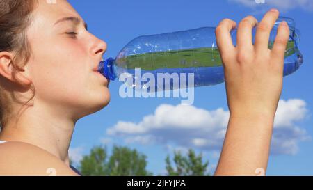 Hermosa niña bebiendo agua contra el cielo azul Foto de stock