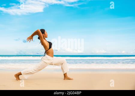 Mujer que practica yoga en la orilla del mar de la playa tropical, deporte dama de pie en la playa hacer ejercicios de yoga Foto de stock