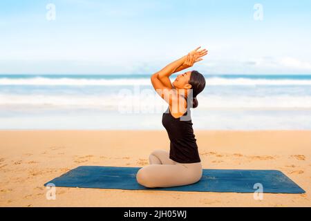 Mujer que practica yoga en la orilla del mar de la playa tropical, deporte dama de pie en la playa hacer ejercicios de yoga Foto de stock