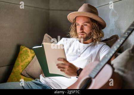 Compositor con guitarra leyendo notas musicales en casa Foto de stock