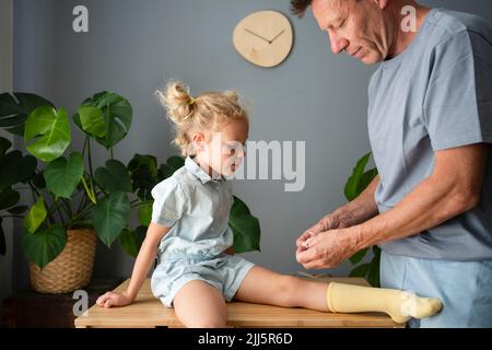 Padre aplicando vendaje en la rodilla de su hija en casa Foto de stock