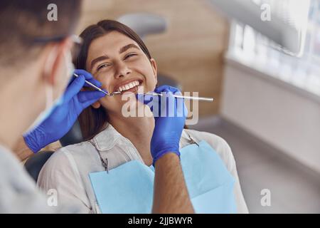 Un doctor profesional está revisando los dientes de la mujer en una clínica dental moderna y ligera Foto de stock