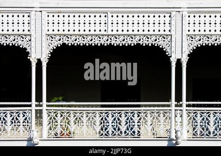 Balcón de hierro forjado decorativo victoriano con una planta pero sobre todo oscuridad detrás de las barandas pintadas de color blanco ornamentadas - fondo Foto de stock