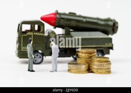 El concepto del presupuesto militar. Sobre una superficie blanca hay figuras de personas, monedas y un vehículo militar de juguete. Foto de stock