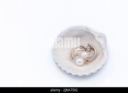 Par de pendientes dorados con perlas que yacen dentro de la concha marina sobre fondo blanco Foto de stock