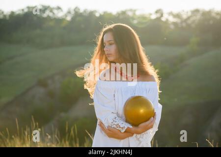 Niña adolescente con una bola gimnástica en el fondo de un barranco. Retroiluminación de atardecer. Foto de stock