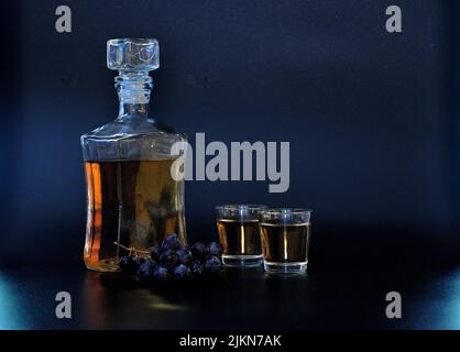 Una botella de grappa, alcohol italiano fuerte, dos vasos y un montón de uvas oscuras sobre fondo negro. Primer plano. Foto de stock