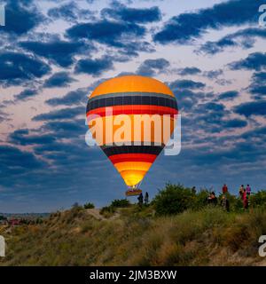 GOREME/TURQUÍA - 30 de junio de 2022: Un globo aerostático vuela sobre los turistas cerca de las colinas de goreme. Foto de stock