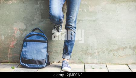Patas de colegiala en jeans azules con mochila de vuelta a la escuela Foto de stock