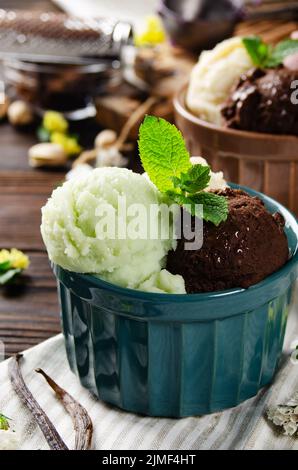 Tres cucharadas de pistacho de vainilla y bolas de helado de chocolate en cuencos de arcilla sobre una mesa de cocina de madera Foto de stock