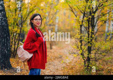 Mujer con gafas se pone de pie y mira la cámara en el fondo del bosque de otoño Foto de stock