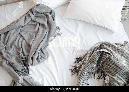 Cama sin hacer con almohada y mantas grises vista superior Foto de stock